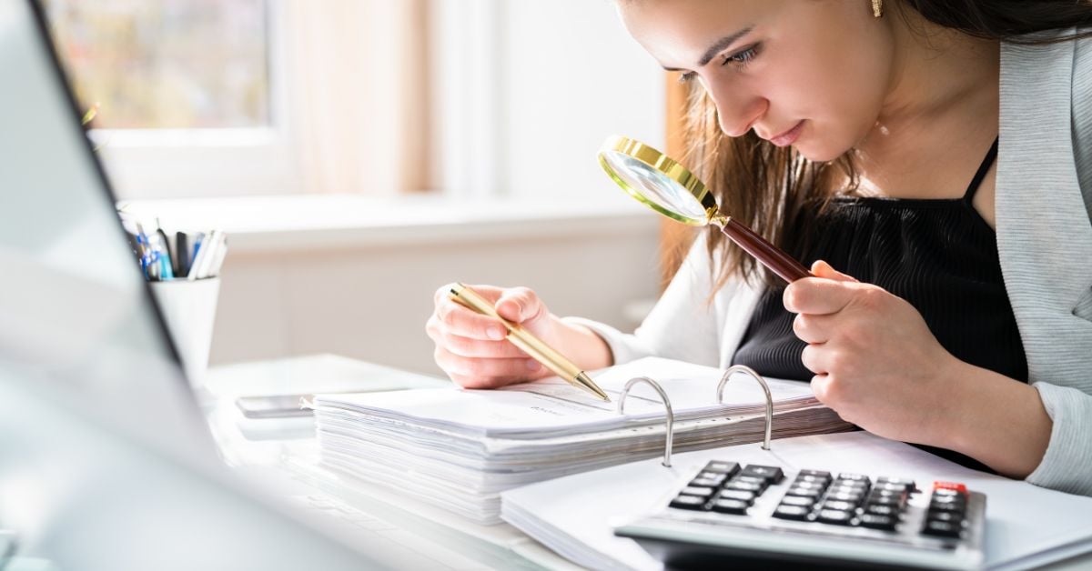 woman looking at financial papers with magnifying glass