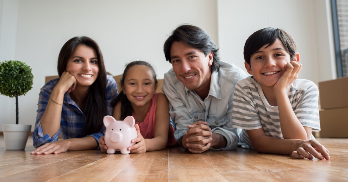 family laying on ground with piggy bank smiling